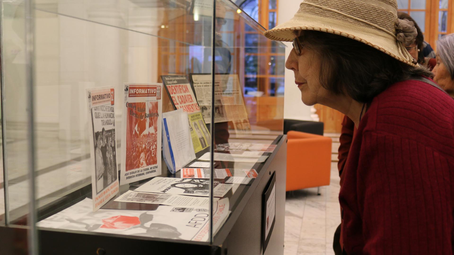 mujer mirando exposición que contiene diarios con información de detenidos desaparecidos 